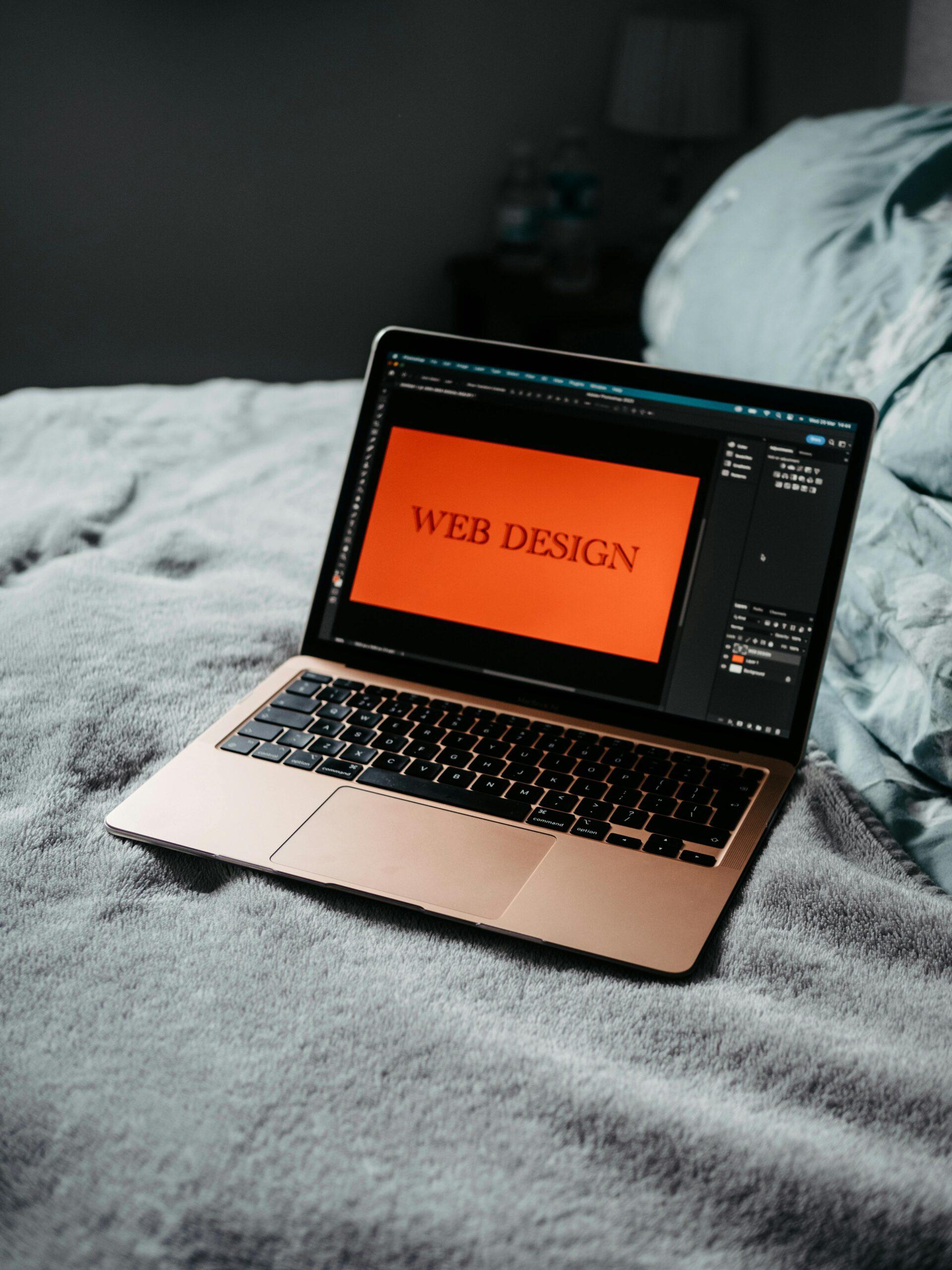 A laptop on a bed showing web design software, creating a cozy workspace.